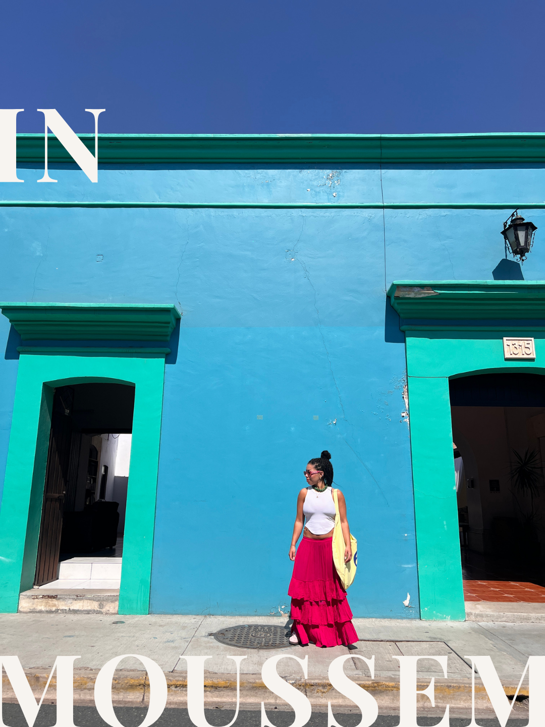 Sarah Moussem in a pink skirt standing in front of a bright blue building in Mexico City